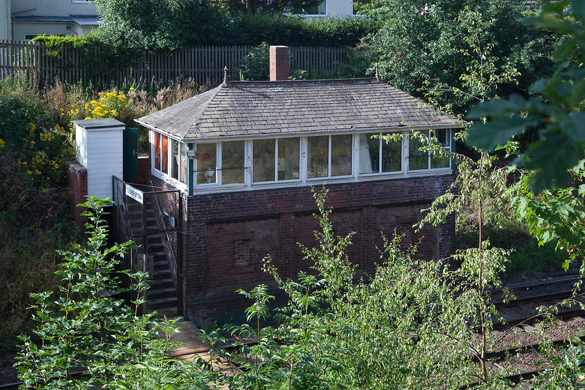 Ulverston signal box (Furness, 1902) 
 Another box that I photographed during my October 1985 survey of the Cumbrian Line. Back then I got a most reasonable shot from track level, I'm not at all sure how I managed it but I may have walked up from the siding that comes off the line to the north? This time, I have had to make do with this shot that found me teetering atop a fence in order to clear the foliage! Ulverston box is a substantial affair opened by the Furness in 1902 and built to their Type 4 design. 
 Keywords: Ulverston signal box