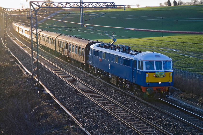 86259, outward leg of The Winter Cumbrian Mountain Express, 07.08 London Euston-Carlisle (1Z86), Milton crossing 
 86259 'Les Ross' (on this side at least!) makes a fine sight as it sweeps around the curve at Milton crossing having just emerged from the relative darkness of Roade cutting. It is leading the outward leg of The Winter Cumbrian Mountain Express that left Euston at 07.08 for Carlisle with the ac electric coming off the train at Carnforth in favour of 45699 'Galatea'. The former LMS Jubilee would then take the train over Shap to Carlisle and southwards over the Settle and Carlisle to Farington Junction where the ac would bring the train back in the evening passing this spot again at 21.15. 
 Keywords: 86259 The Winter Cumbrian Mountain Express 07.08 London Euston-Carlisle 1Z86 Milton crossing Less Ross Peter Pan WCR