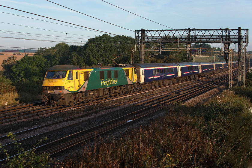 90045, CS 19.50 Fort William, 21.43 Aberdeen & 20.45 Inverness-London Euston (1M16, 6E), Roade Hill 
 Some three months after they should have been withdrawn in favour of the Mk. V coaches, the Mk. III sleepers are still in front-line use on the up and down Highland services. The 1M16 up Highland sleeper passes Roade Hill with 90045 leading the train. It was a stunning summer morning that made the walk across the fields from home, complete with my full-sized step ladder, worthwhile. The ladder is needed to get me above the palisade fencing but I have had to devise a protective cover that attaches over the spikes having nearly removed an index finger some years ago on one. 
 Keywords: 90045 19.50 Fort William 21.43 Aberdeen 20.45 Inverness-London Euston 1M16 Roade Hill