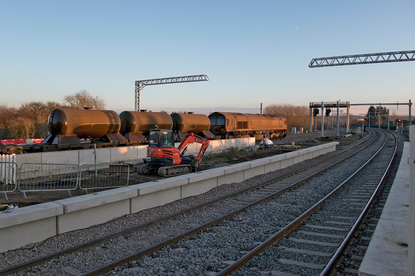 66143, 11.53 West Hampstead North-Toton, Wellingborough station 
 With the water tankers glistening in the very late afternoon sunshine, 66143 brings up the rear of the 11.53 West Hampstead to Toton RHT train as it drifts into Wellingborough station approaching a red signal. Due to it coming to a halt the water jets have been switched off to avoid damage to the track from the extremely high-pressure jets that clear autumn detritus from it. This view clearly shows the extensive platform extensions to the south of the station. 
 Keywords: 66143 11.53 West Hampstead North-Toton Wellingborough station RHT railhead treatment train