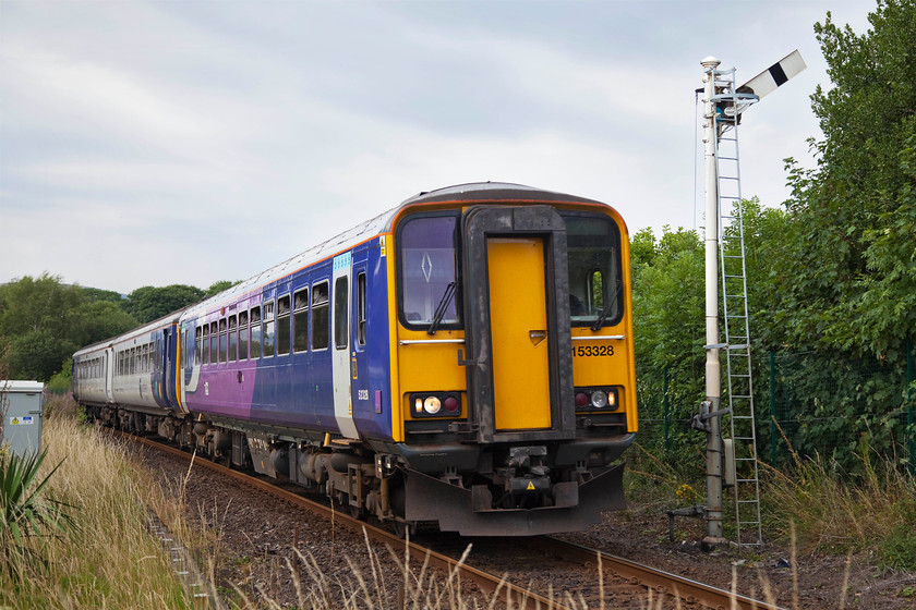 153328 & 156471, NT 16.48 Windermere-Oxenholme Lake District (2C15, 2L), Burneside SD503954 
 Having run earlier down to Windermere, 153328 and 156471 return with the 16.48 to Oxenholme or 'Oxenholme Lake District' as Network Rail and the TOCs persist in calling it. The combo is seen approaching Burneside level crossing passing the protecting up home semaphore. The train has just left Burneside station that is just around the corner out of shot behind the grey box. 
 Keywords: 153328 156471 2C15 Burneside SD50395