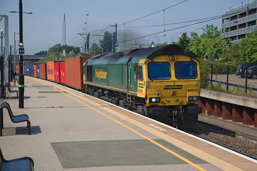 66591,12.12 Lawley Street-London Gateway (4L46), Milton Keynes station 
 66591 produces a trail of black exhaust working the the 4L46 12.12 Lawley Street to London Gateway Freightliner. It's days like this that make the driver's job in a 66 a little uncomfortable as they have no air conditioning with many complaints and consequential union involvement. 
 Keywords: 66591 12.12 Lawley Street-London Gateway 4L46 Milton Keynes station