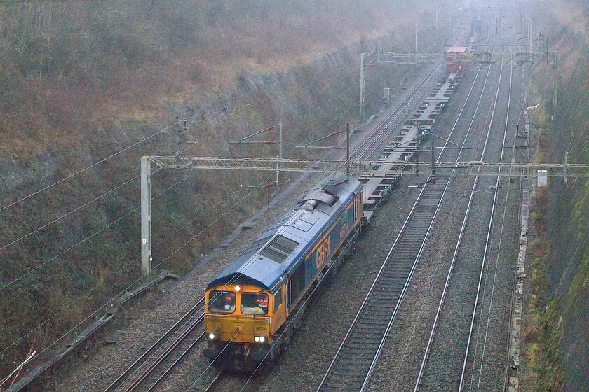 66754, 11.39 London Gateway-Hams Hall (4M47, 6E), Roade cutting 
 Appearing through the murk 66754 'Northampton Saints' passes through Roade cutting working the 4M47 11.39 London Gateway to Hams Hall service. 
 Keywords: 66754 11.39 London Gateway-Hams Hall 4M47 Roade cutting GBRf Northampton Saints