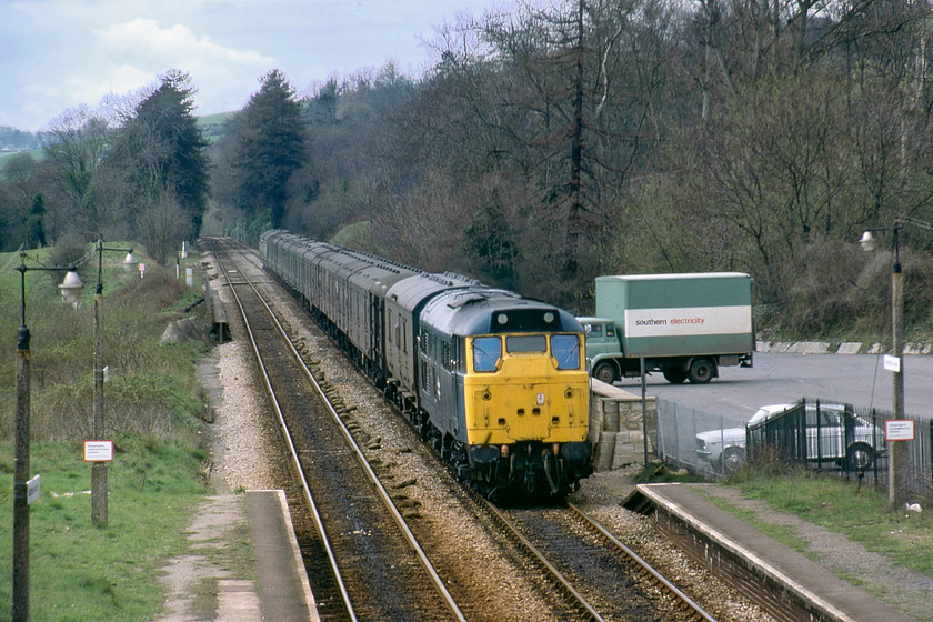 31254, up parcels working, Bradford-on-Avon station 
 Using my Helios 135mm telephoto lens at Bradford-on-Avon has compressed the view looking along the Avon Valley towards Bath. Locally based at Bristol Bath Road, 31254 was a regularly spotted member of the class but not for much longer as it was withdrawn seven months after this picture was taken. It is seen hauling a parcels working in the Westbury direction, a train made up of a mixture of parcels vans including an LMS and Southern variant. Notice the relatively empty station car park, a scene very unlikely today. The Bedford TK lorry belonging to Southern Electric and the white Austin Maxi will, like the class 31, will be long-gone! 
 Keywords: 31254 parcels working Bradford-on-Avon station