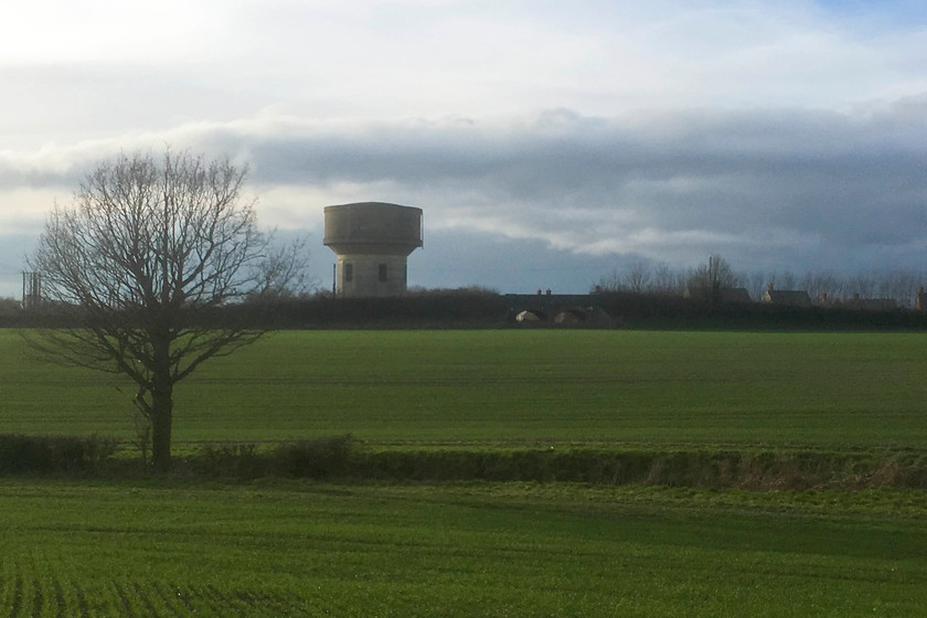 Former SM & J bridge, Ashton Road, Roade 
 With one of Roade's iconic water towers dominating the skyline, the bridge that carries Ashton Road that marks the route of the SM & J railway can be made out. The route of the line went across the field towards the right of the image. This is a very similar view to the one from my house and is something I wake up to every morning! The WCML is just behind the water tower where the SM & J crossed on what was colloquially referred to as the 'Tin Bridge'. 
 Keywords: SM & J bridge Ashton Road Roade