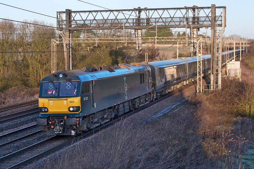 92023, 00.14 Glasgow Central-London Euston sleeper test run (3Z11), Roade Hill 
 A bitterly cold morning is just beginning to warm up a bit as the sun rises but, unfortunately, it is not quite high enough to illuminate the front and side of the locomotive as I had hoped; give it a week or so and it would have done so. Caledonian Sleeper's 92023 brings a rake of the new sleeper stock past Roade Hill just south of Northampton. This 3Z11 left Glasgow Central at 00.14 and after an extended layover at Carstairs, it headed south to Euston. Unfortunately, it arrived some 22 minutes late as it was pathed on the down slow lines as it approached the capital. As the train passed I only got very limited glimpses but the stock looked very smart. The only odd thing, and it can be seen in this picture, is that there's a lack of covers to the underbody. All the various equipment is fully exposed and painted a grey /white colour that will deteriorate very quickly in service. I would go so far as to say that the underbody reminded me of the Mk. II stock that BR introduced in the 1970s! Andy and me are planning to take the sleeper to Scotland for our summer trip this year, the question is, will it be in the Mk. IIIs or will it be in this new stock? 
 Keywords: 92023 00.14 Glasgow Central-London Euston sleeper test run 3Z11 Roade Hill