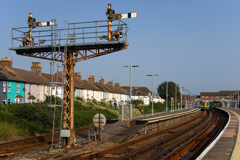 377320, SN 16.55 Littlehampton-Portsmouth & Southsea (2S28, 7L), Littlehampton station 
 In typical Southern style latticed bracket signal housing arms 0036 (platform 3) and 0033 (platform 4) is seen against a brilliant blue late summer sky at Littlehampton. The sea air has not been kind to the metalwork with evidence of considerable corrosion. This is one of the reasons stated by Network Rail for their replacement both here and at nearby Bognor Regis describing the signalling infrastructure as 'life expired'. It is all very much on borrowed time so will not be around for very much longer. In the background, 377320 is seen about to work the 2S28 16.55 all-stations service to Portsmouth and Southsea, a train that I would take as far as Barnham. 
 Keywords: 377320 16.55 Littlehampton-Portsmouth & Southsea 2S28 Littlehampton station Southern Electrostar