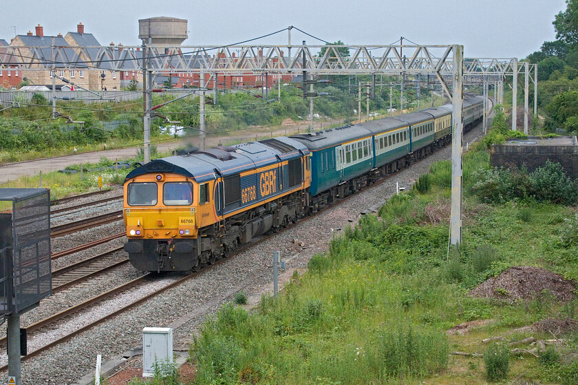 66768, 13.08 Wembley Yard-Burton-ot-Wetmore (5Z64, 117L), site of Roade station 
 Having been waiting on this bridge at Roade for some time it had become clear that there were problems somewhere south. Indeed, for the second day running there were signalling issues at Milton Keynes with all trains appearing to have been stopped with every signal on OpenTrainTimes showing red. With Sunday evening dinner time fast approaching I was on the verge of heading for home when 5Z64, which had been stationary for ages between Milton Keynes and Bletchley, was on the move again. To make it even more interesting, when the 13.08 Wembley Yard to Burton-ot-Wetmore ECS working got to Hanslope it was put on the fast line to avoid a very congested Northampton I suspect. Now, nearly two hours late, the superb retro. Mk. II set used for railtour duties the previous day are seen passing Roade hauled by a customary smartly presented GBRf 66768. 
 Keywords: 66768 13.08 Wembley Yard-Burton-ot-Wetmore 5Z64 site of Roade station Intercity Mk.11