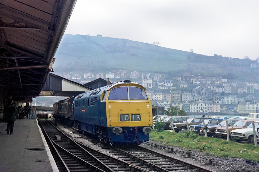 D1013, stabled, Kingswear station 
 D1013 'Western Ranger' rests at Kingswear station having worked a return train to Paignton with D1062 'Western Courier' having taken over. Just look at the line of fine 60s and 70s cars lined up in the car park, close examination reveals not a foreign interloper almost them! 
 Keywords: D1013 stabled Kingswear station