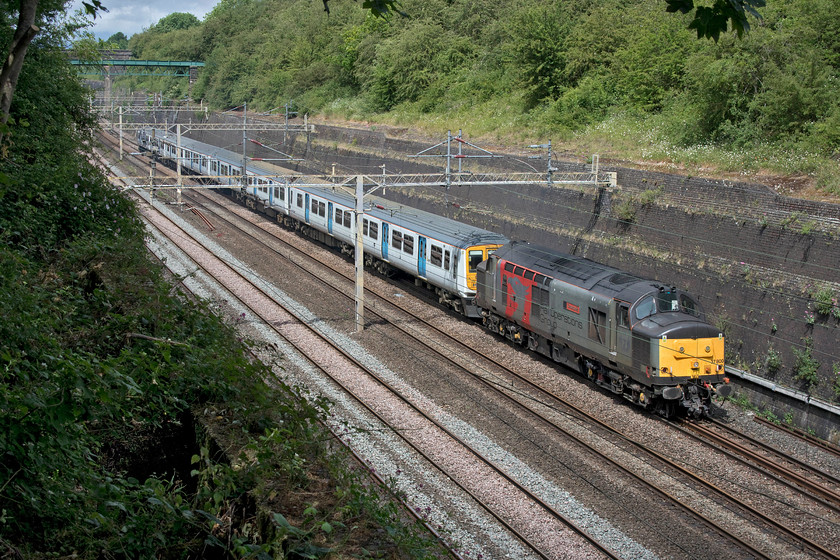 37800, 319373 & 319009, 10.18 Long Marston-Eastleigh Arlington (5Q86, 1E), Roade cutting 
 Again lucky with the sun as it had just stopped raining, 37800 'Cassiopeia' is seen working hard through Roade cutting towing 319373 and 319009. The two former Thameslink units were being taken from storage at Long Marston to Eastleigh's Arlington plant for attention running as 5Q86. It is taking a very strange route from Long Marston, located just north of the Cotswold line, via Worcester, Lickey, St. Andrew's Junction, down the WCML to London (via Kensington) thence to Eastleigh. There are other far more straightforward routes that this train could have taken so I am somewhat intrigued as to why this two hundred and forty-two miles journey was chosen....advice anybody?

There is an audio recording of this event on my youtube channel, see.... https://www.youtube.com/watch?v=gRZ1XSRBoOU 
 Keywords: 37800 319373 319009 10.18 Long Marston-Eastleigh Arlington 5Q86 Roade cutting Cassiopeia