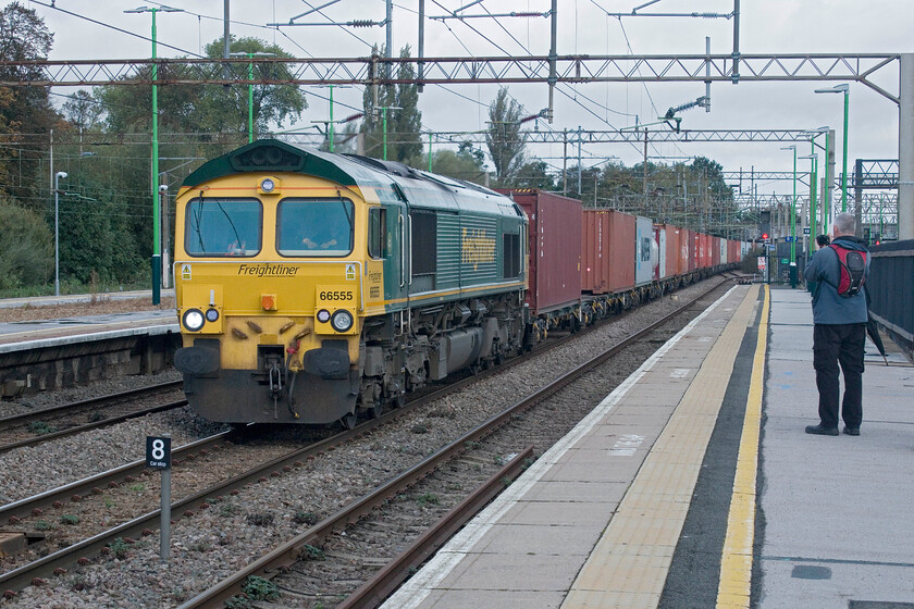 66555, 06.15 Trafford Park-Felixstowe North (4L97, 67L), Northampton station 
 Complete with his umbrella at the ready one of the gathered enthusiasts at Northampton station captures 66555 passing south leading the 06.15 Trafford Park to Felixstowe Freightliner. This service was fully loaded with boxes unlike the next freight to pass....... 
 Keywords: 66555 06.15 Trafford Park-Felixstowe North 4L97 Northampton station Freightliner