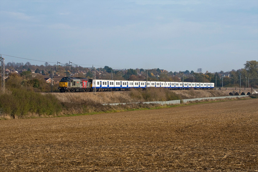 37800, 315846 & 315845, 05.22 Ilford EMUD-Kingsbury Sidings (5Q66), Wilsons Crossing 
 Any train heading for Kingsbury is only going there for one reason; this one is no exception! 37800 'Cassiopeia' leads a pair of off-lease TfL Rail class 315s for scrapping. The leading unit is 315846 followed by 315845 previously named 'Herbie Woodward'. The whole train looks, considering its fate, rather smart in the autumn sunshine as it passes Wilson's Crossing to the north of Northampton running, by this stage over one hundred minutes late. 
 Keywords: 37800 315846 315845 05.22 Ilford EMUD-Kingsbury Sidings 5Q66 Wilsons Crossing