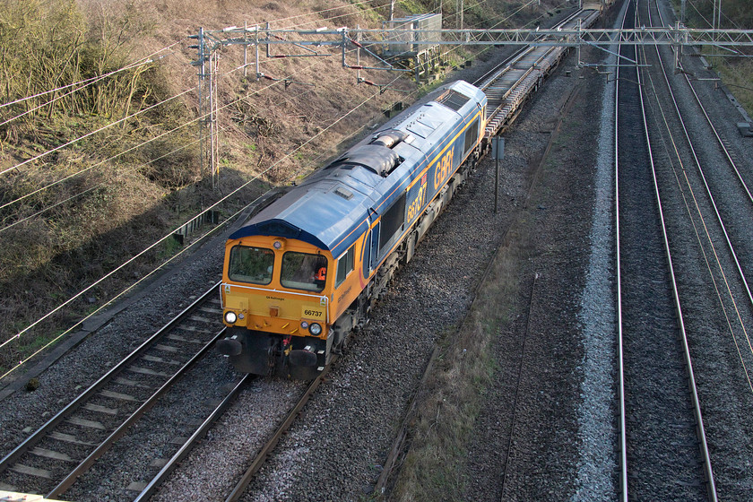 66737, 13.15 Milton Keynes Central-Bescot (6G51, 6E), Victoria bridge 
 66737 'Lesia' passes Victoria bridge just south of Roade with the returning 13.15 Milton Keynes to Bescot engineering train that actually started from Bletchley with the 66 running round after initially heading south. 66737 is named 'Lesia' after the wife of GBRf's MD John Smith. Eagle-eyed spotters will notice the extra large 37 in the number. Apparently, the explanation of this is that in the Smith household there is a running joke that Mrs. Smith always claims to be thirty-seven when asked her age. So to maintain this her husband chose one of his locomotives to continue the joke; a nice story if it's true! 
 Keywords: 66737 13.15 Milton Keynes Central-Bescot 6G51 Victoria bridge Engineering train Lesia