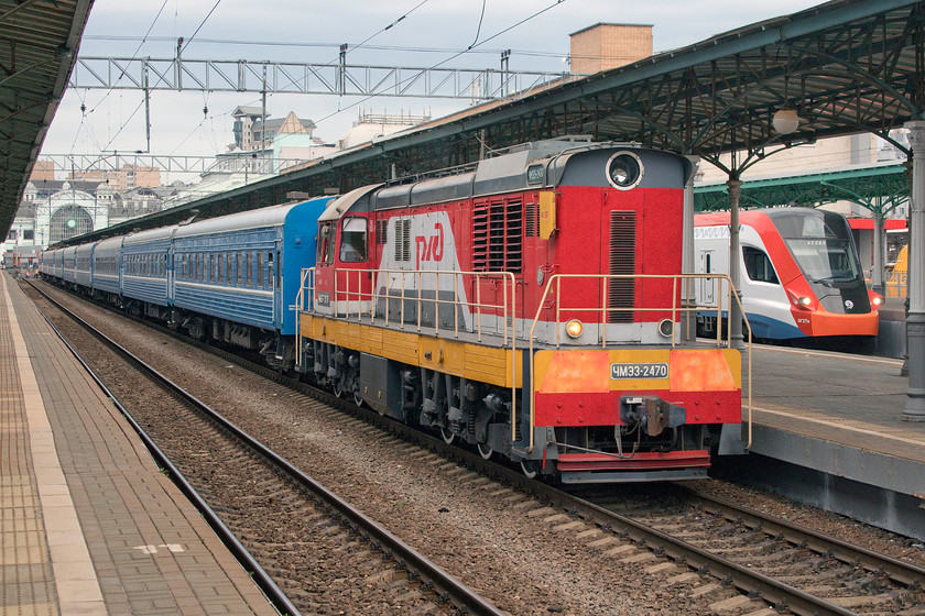 CMZ3-2470, station pilot & EG2TV0005, unidentified Usovo working, Moscow Belorussky station 
 Station pilot CMZ3-2470 carefully reverses the stock for the 22.11 to Minsk into Moscow Belorussky station. The driver of the shunter was being guided by a pilot standing in the vestibule of the last coach communicating via radio. Behind the shunter is one of the new Ivolga EG2TV urban EMUs. These have been introduced as part of a joint programme between Moscow city, the regional governments, Russias Ministry of Transport and RZD on a number of new-build lines linking large parts of greater Moscow and linking into the Metro system. A grand and joined-up plan that is beeing delivered on-time, Cross Rail please take note! 
 Keywords: CMZ3-2470 station pilot EG2TV0005 Usovo working Moscow Belorussky station