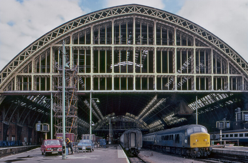 45143, 17.00 London St. Pancras-Bedford (2G17), London St. Pancras station 
 A wide angled photograph of the grand train shed at St. Pancras that is seen undergoing some British Rail 'style' improvements! By now the decision to save the station from demolition had been made but BR simply did not have the funding to complete a full and much-needed restoration so there was a repair and make do approach until the much-heralded transformation that we are all so familiar with commenced in 2002. In this view, 45143 '5th Royal Inniskilling Dragoon Guards' is waiting to depart leading the 2G17 17.00 commuter service to Bedford. There were a number of locomotive hauled morning and evening peak services (excusing the pun!) composed of a scratch set of Mk. 1stock hauled by a locomotive of some kind. Notice the contractors' cars parked on the platform near their scaffolding. There is a blue Vauxhall Viva HC Firenza Coup and a now ultra-rare red 'N' registered Fiat 124 Special with its twin headlights and period bumper-mounted fog or driving lamps. Because of using the wide-angled lens, this photograph did need a fair amount of Photoshop tweaking to straighten out the curved verticals and horizontals producing what I think is a great result! 
 Keywords: 45143 17.00 London St. Pancras-Bedford MIdland 2G17 London St. Pancras station 5th Royal Inniskilling Dragoon Guards Peak