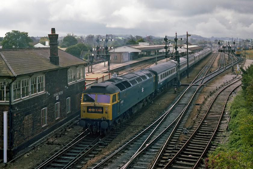 47537, unidentified up working, Westbury north 
 A classic location at the eastern end of Westbury station that has been a firm favourite for many photographers over the years. Thankfully, its a cloudy day becuase if the sun had been out this shot would have been straight into it. It shows 47537 leaving the station leading an unidentified up working. 47537 is still on the network today (2018) as a maroon WCRC locomotive numbered 47772. Notice in the background, the massive number of locos. on-shed at Westbury Depot. It looks to be packed with class 37 and 47 locomotives that, as it was a Saturday, would be standing idle awaiting their next job. 
 Keywords: 47537 unidentified up working Westbury north