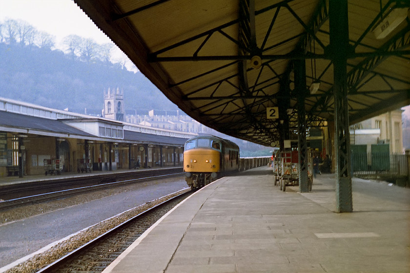 46011, up ballast working, Bath Spa station 
 The shutter has been pressed very early but with the very limited fast shutter speed on the Exa camera of only 1/150th sec. if it had been any closer motion blur would have spoilt the image; I was thinking ahead! The image shows 46011 on an up PW working of some kind, probably heading towards Westbury. Apart from the train, this picture is full of interest. On the far right is the former up facing bay platform. Sitting above the down canopy is the remains of the former signal box that commanded a lofty position above the station giving good views in all directions. In the background is the tower of St. Mark's church. In 2014 I stood in s similar position and took a photograph of 158960 leaving the station, the scene is remarkably similar, see..... https://www.ontheupfast.com/p/21936chg/29945957604/x1-158960-gw-14-30-cardiff-c-portsmouth 
 Keywords: 46011 up ballast working Bath Spa station