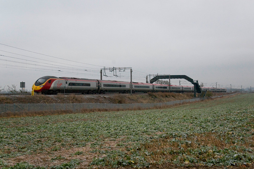 Class 390, VT 07.20 London Euston-Manchester Piccadilly (1H09), Blisworth 
 In the February gloom, a class 390 passes Blisworth forming the 07.20 Euston to Manchester. The field in the foreground is just turning green as the summer's oilseed rape emerges from the soil; it's hard to imagine that this scene will be one of bright yellow within about three months! 
 Keywords: 07.20 London Euston-Manchester Piccadilly 1H09 Blisworth