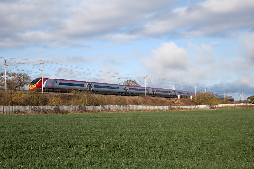 390020, VT 04.26 Glasgow Central-London Euston (1M21), Milton Crossing 
 In the early morning spring sunshine 390020 speeds south with the first up Glasgow Central working of the day that left in the darkness at 04.26. The picture is taken near to Milton Crossing between the villages of Blisworth and Roade on the Weedon loop of the WCML. If some developers have their way, this scene will change beyond all recognition as a huge railfreight and warehousing facility is to built on this land. 
 Keywords: 390020 04.26 Glasgow Central-London Euston 1M21 Milton Crossing