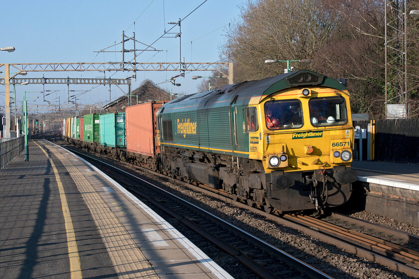 66571, 12.16 Lawley Street-London Gateway (4L46, 2E), Kings Langley station 
 Freighliner's 66571 at speed through Kings Langley station leading the 12.16 Lawley Street to London Gateway. The former goods shed, now somewhat ivy-clad, can be seen rising just above the front two boxes of the train. 
 Keywords: 66571 12.16 Lawley Street-London Gateway 4L46 Kings Langley station