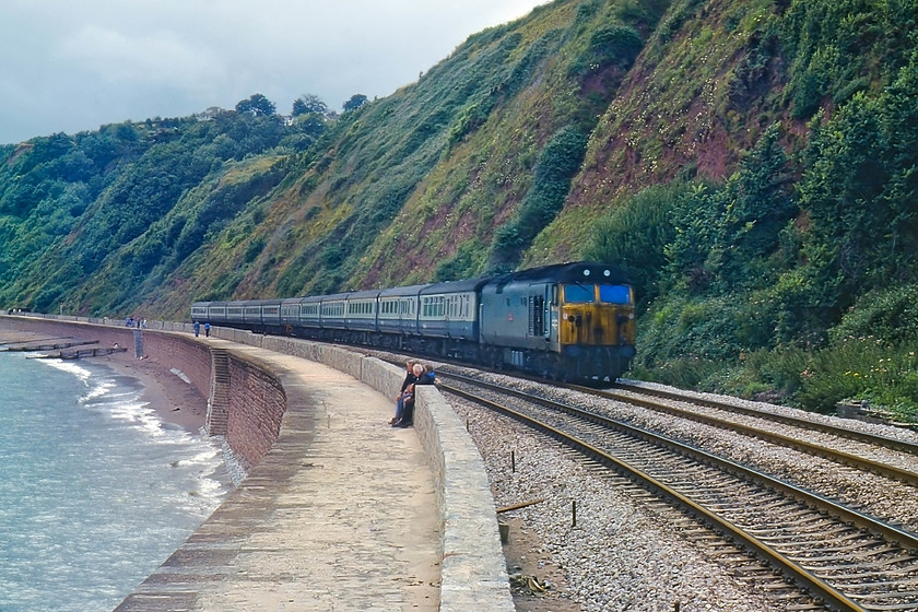 50039, 10.56 Penzance-London Paddington, The Cornish Riviera (1A81), Parson`s Tunnel 
 Looking west from Parsons Tunnel, a very tatty 50039 'Implacable' takes the 1A81 10.56 Penzance to London Paddington, the up Cornish Riviera along the sea wall. The condition of many class 50s by this time left a lot to be desired. They were becoming increasingly unreliable and unloved by the drivers and maintenance staff alike, so BR set about a programme of refurbishment. The first to be out-shopped from Doncaster was 50006 'Neptune' in November 1979. It was in standard BR blue with the hole for the centre headlight plated over, allegedly due to a shortage of parts. 
 Keywords: 50039 10.56 Penzance-London Paddington The Cornish Riviera Parson`s Tunnel