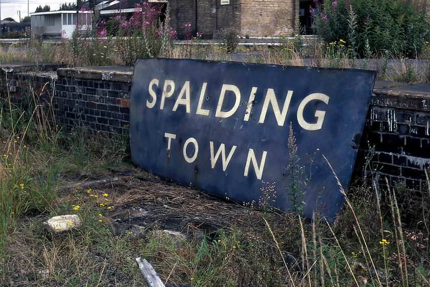 Enamel, Spalding Station 
 Whilst Graham and I were exploring the delights of Spalding station we stumbled across this enamel sign laying on its front in the undergrowth on next to a closed platform. It was a non-flanged British Railways (ER) large sign that had simply been tossed away I suspect when the station received its BR corporate identity black and white signage. Interestingly, the sign refers to Spalding Town station suggesting that another station existed; there was no other so why it was simply not called Spalding (as is the case today) I do not know? We did toy with the idea of saving it but it would not fit in the back of the Mini and we did not have the roof rack so reluctantly we returned it to where we found it; I wonder if a Spalding resident rescued it and if it still exists? 
 Keywords: Enamel Spalding Station