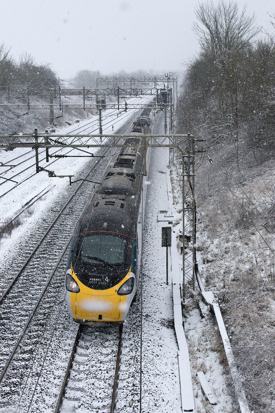 Class 390, VT 10.49 London Euston-Wo;verhampton (9G06, 37L), Victoria bridge 
 A photograph of a Pendolino taken from this position would normally find me identifying the set from the small car number written on the section of raised roof near to the pantograph. However, due to the build-up of snow, this is not possible so this one remains unidentified. The Avanti West Coast 10.49 Euston to Wolverhampton service passes Victoria bridge just south of Roade on time but things were to go badly wrong in just over twenty miles at Rugby with all trains suffering from delays caused by the inclement weather. 
 Keywords: Class 390 VT 10.49 London Euston-Wolverhampton 9G06 Victoria bridge Avanti West Coast Pendolino