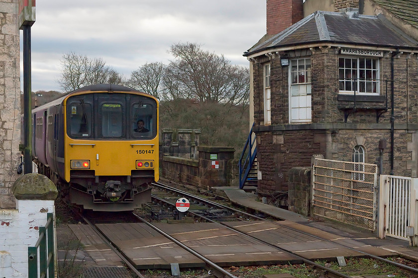 150147, NT 13.11 York-Leeds, Knaresborough station 
 The train guard watches me from the rear cab of 150147 as it leaves Knaresborough station working the 13.11 York to Leeds. The train is just about to cross Knaresborough's magnificent viaduct and is passing the interesting North Eastern 1873 signal box that is integrated into the row of stone-built houses. 
 Keywords: 150147 13.11 York-Leeds Knaresborough station