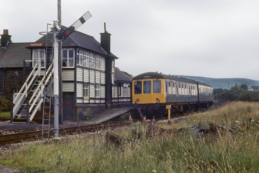 M56250 & M50947, 14.40 Barrow-in-Furness-Sellafield, Foxfield station 
 A Derby built Class 108 two-car DMU leaves Foxfield station working the 14.40 Barrow-in-Furness to Sellafield local stopper. Notice the drop lights in the doors have bars across the openings to avoid heads being leaned out. This is because these DMUs operated through a number of very narrow bore tunnels on the Cumbrian Coast line, for example, just south of Whitehaven. These class 108s were based at Carlisle and were dedicated for use on this line. At the time of writing, the glorious 1879 Furness signal box is still in use, indeed, I took a very similar picture during a visit in 2013 but there was no first-generation DMU featuring in that particular image, see.... https://www.ontheupfast.com/p/21936chg/30061915079/x35-foxfield-signal-box-furness-1879 
 Keywords: M56250 M50947 14.40 Barrow-in-Furness-Sellafield Foxfield station