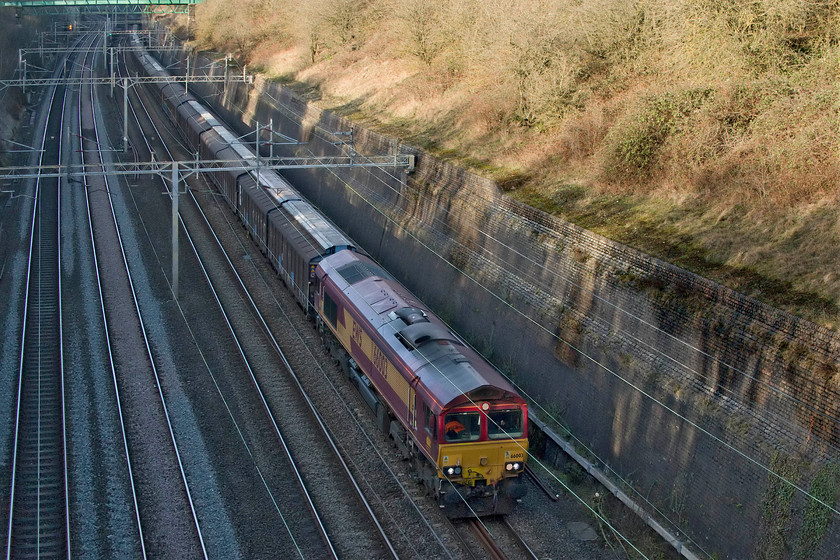 66003, 14.41 DIRFT-Dollands Moor (6O67, 2L), Roade cutting 
 I was not going to hang about to see the passage of the 6O67 empty water bottle train from Daventry back to Dollands Moor but I am very glad that I did. It was being hauled by 66003 that was a photographic cop and it is seen hauling the train through Roade cutting. Remarkably, 66003 has worn this livery throughout its whole life since it arrived in the UK during August 1998. Close examination reveals that the EWS three besties logo is still on the cab end despite the operator not existing since 2007 when it was bought by Deutsche Bahn. 
 Keywords: 66003 14.41 DIRFT-Dollands Moor 6O67 Roade cutting