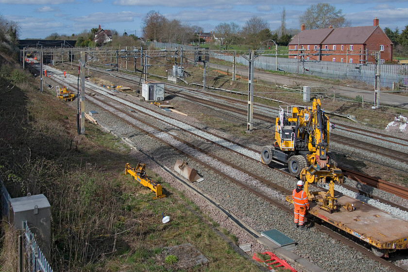 Engineering work, site of Roade station 
 A Dooson Ultimate DX270 on hire from TXM Plant (Wigan) sits on the up fast line at the site of Roades former station undertaking some work associated with re-ballasting. In the distance, past the A508 road bridge, 66418 Patriot - In Memory of Fallen Railway Employees waits at the head of a short ballast train to inch forward to deposit more stone. 
 Keywords: Engineering work, site of Roade station