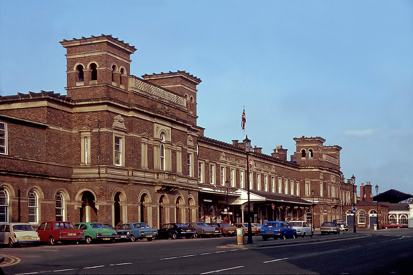 Frontage, Chester station 
 Chester station's Italianate frontage was designed by the renowned architect Francis Thompson and was opened 1848. With its three hundred and five-metre long two-storey faade built out of Staffordshire blue brick and pale grey Storeton sandstone, it is undoubtedly an impressive structure that was making a real statement of intent by Robert Stephenson's new Chester and Holyhead Railway! I took a similar photograph to this 1981 view when I revisited in 2021, see.... https://www.ontheupfast.com/p/21936chg/30021093933/frontage-chester-station The lineup of 1970s cars, is notable for the fact that it includes just two foreign interlopers in the form of a Datsun Sunny and a Daf 33. The remaining fourteen home-built cars include no fewer than six Fords such was their dominance at that time! Our trusty Austin 1100 (UVJ 129J) is seen parked to the extreme left in the line up. 
 Keywords: Frontage Chester station