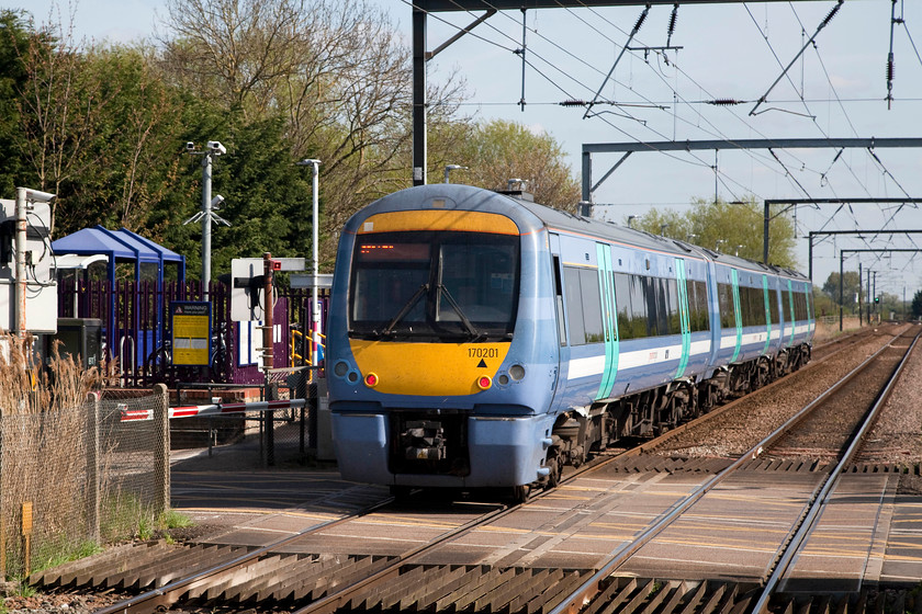 170201, GA 10.12 Cambridge-Norwich (1K66, 1L), Waterbeach station 
 170201 arrives at Waterbeach station working the 10.12 Cambridge to Norwich 1K66 service. As can be seen here, Waterbeach is has a split platform arrangement with the level crossing over the minor road dividing them. Judging by the number of parked cars in the wholly inadequate car park and the abandoned vehicles left on the surrounding roads, Waterbeach attracts a lot of commuters! Despite the sunny spring day, it was chilly with a keen wind blowing. 
 Keywords: 170201 1K66 Waterbeach station