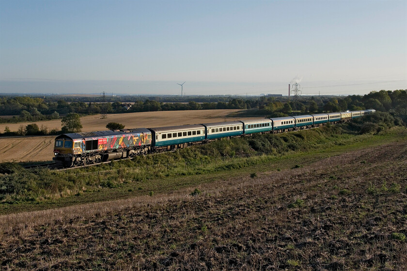 66718, outward leg of The Bluebell Railway, 06.07 East Midlands Parkway-East Grinstead Sidings (1Z80, 7L), Lidlington SP978384 
 66718 'Peter, Lord Hendy of Richmond Hill, of Imber in the County of Wiltshire' leads the outward leg of UK Railtour's The Bluebell Railway charter. past Lidlington in Bedfordshire. The charter started out from East Midlands Parkway and would end up at East Grinstead and would feature some Class 73 haulage later on in the day. This slightly elevated view gives a good view of the Vale of Marston looking northeast toward Bedford. In years past the scene would have been dominated by a number of tall chimneys associated with the brickwork industry that was the backbone of the economy of the area. Like so many primary industries in the UK they have fallen by the wayside with most bricks now imported. Unfortunately, the return charter was thrown into chaos when it was inadvertently re-routed via the WCML rather than the Marston Vale line causing a long and awkward diversion via a reversal at Nuneaton as well as passengers for Bedford and Kettering having to be bussed and taxied to their start points. 
 Keywords: 66718 The Bluebell Railway 06.07 East Midlands Parkway-East Grinstead Sidings 1Z80 Lidlington SP978384 Peter, Lord Hendy of Richmond Hill, of Imber in the County of Wiltshire UK Railtours