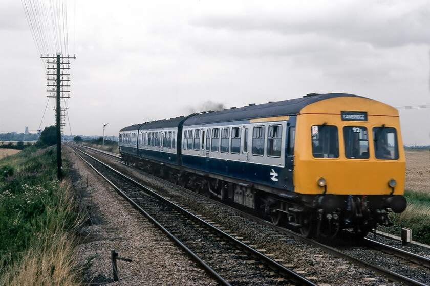 Class 101 DMU, 13.36 Peterborough-Cambridge, West River 
 A smart-looking Class 101 speeds across the flatlands south of Ely with the 13.36 Peterborough to Cambridge service. Often referred to as The Ship of the Fens, one of the finest medieval wonders of the world in the form of Ely Cathedral is seen on the skyline locating this image to a dead-end road crossing known as West River near the village of Little Thetford. The home signal that the train has just passed is controlled by the Great Eastern signal box on the opposite side of the line to me over my right shoulder. Apologies for the blurring of the train caused by me not selecting a fast enough shutter speed on my Pentax ME Super which could go up to 1:2000/sec. that was pretty good for a consumer SLR from the early 1980s! 
 Keywords: Class 101 DMU 13.36 Peterborough-Cambridge West River First generation DMU