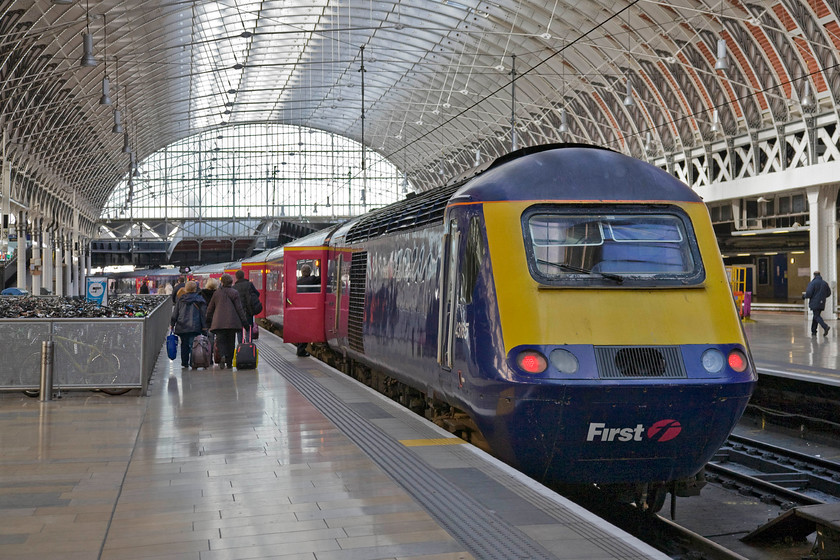 43165, GW unidentified down working, Paddington station 
 Passengers make their way along platform seven to find their seats aboard an unidentified down First Great Western service. The train will be powered at the rear by 43165 that was one of the later power cars introduced from the summer of 1982 to work the NE/SW services. In this particular case, this power car was part of set 253043. Notice the brilliant shine on the platform slabs reflecting every bead of light that falls on them, the buffers have certainly been doing their stuff here on platform seven! 
 Keywords: 43165 Paddington station First Great Western HST