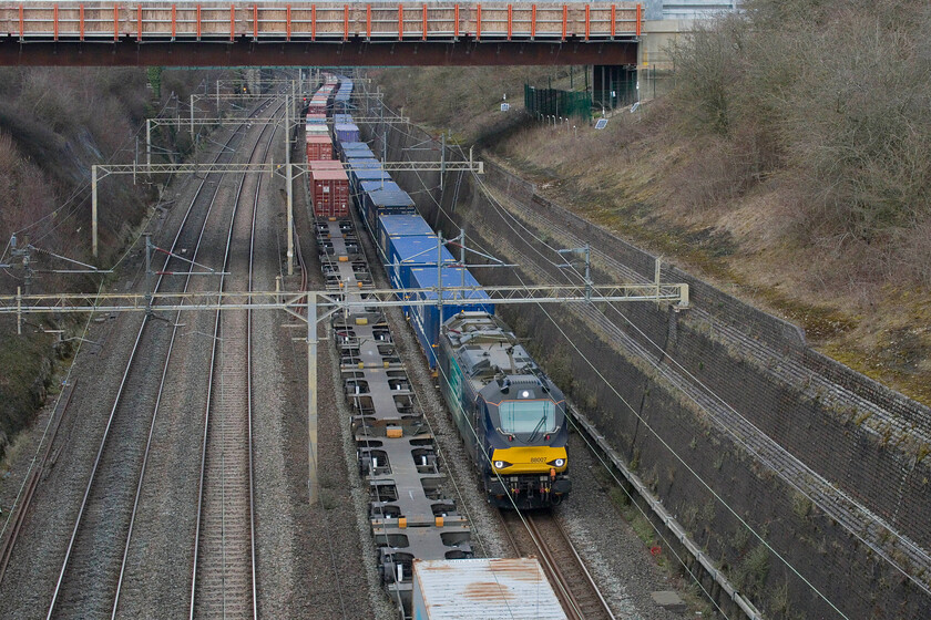 88007, 13.37 DIRFT-Tilbury (4L48, RT), Roade cutting 
 With the 4M63 Felixstowe to Trafford Park Freightliner just heading north through Roade cutting 88007 Electra passes southwards leading the 4L48 Tesco Express 13.37 Daventry (DIRFT) to Tilbury. With this being electric-led rather than a Class 66 its progress from Northampton to this spot nearly caught me out with it arriving far more quickly than would normally be the case. I was lucky that I was able to position the subject adjacent to a gap in the boxes on the northbound train! 
 Keywords: 88007 13.37 DIRFT-Tilbury 4L48 Roade cutting Electra