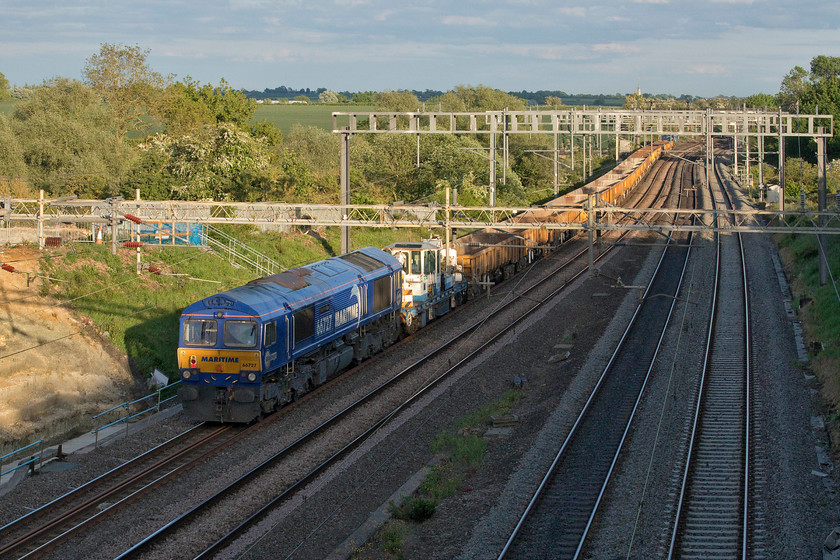 66727, 17.38 Bescot-Camden Junction (7G52, 19L), Ashton Road bridge 
 This is a photograph that resulted in cold chips for yours truly! I told my wife that I would only be twenty minutes as I walked out from home, with my ladder, to capture the passage of the 17.38 Bescot to Camden Junction infrastructure working as it approached Northampton. However, in their wisdom control held it and held it again for a procession of diverted Pendolinos and locals to pass at the station. Eventually, it got underway and is seen running thirty minutes late just south of Roade heading south with 66727 'Maritime One' dead at the rear with 66711 'Sence' doing the work at the front. Notice the track machine tucked in at the rear of the consist. Also, notice the spire of Hanslope's St. James the Great church catching the evening sun against a dark sky. 
 Keywords: 66727 17.38 Bescot-Camden Junction 7G52 Ashton Road bridge Maritime One