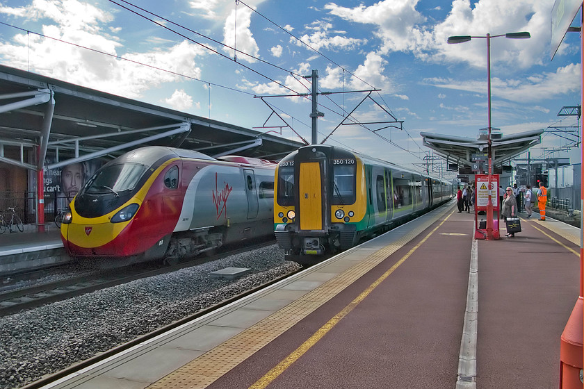 350120, LM 14.02 Crewe-London Euston (1U34) & 390049, VT 14.35 Manchester Piccadilly-London Euston (1A44), Rugby station 
 Breaking the photographic rules by looking into the warm afternoon summer sunshine but under a 'big' sky, 390120 passes through Rugby with the 1A44 14.35 Manchester Piccadilly to Euston train. Meanwhile, 350120 waits for the Pendolino to clear before it will continue its journey behind it as the 14.02 Crewe to Euston train. My wife and I had just alighted from the London Midland Desiro having travelled down from Stafford on it. 
 Keywords: 350120 14.02 Crewe-London Euston 1U34 390049 14.35 Manchester Piccadilly-London Euston 1A44 Rugby station