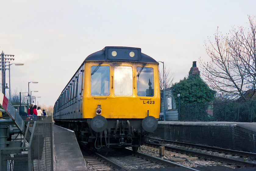 L423, unidentified Bedwyn-London Paddington working, Kintbury station 
 As the barriers raise at Kintbury station, a class 117 DMU set number L423 comes to a halt. There appears to a good a good number of passengers waiting to board the unidentified Bedwyn to London Paddington working. Notice the timber clad GW waiting room on the other platform slowly being enveloped by ivy. 
 Keywords: L423 unidentified Bedwyn-London Paddington working Kintbury station