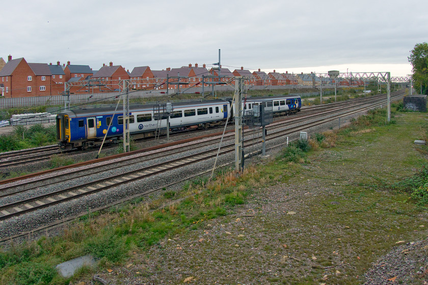 156452, 09.40 Wolverton Centre sidings-Newton Heath TMD (5N31, 7E), site of Roade station 
 A total 'grab shot' of the second Northern return working of the morning passes the site of Roade's former station. 156452 was working the 5N31 09.40 Wolverton works to Newton Heath. This working had caught me unawares as I was returning from the garage shop hence the poorly composed photograph that includes plenty of the new houses on the former Pianoforte site in the vista. Notice the Pendolino fast approaching from the south that could have spoilt the photograph. 
 Keywords: 156452 09.40 Wolverton Centre sidings-Newton Heath TMD 5N31 site of Roade station Northern