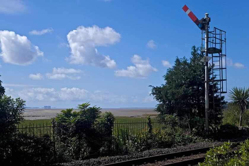 Down starter, Grange-over-Sands 
 With Grange-over-Sands signal box switched out the signals remain pulled off. The down starter is no exception and is viewed from the delightful Ornamental Gardens. The vast expanse of Morecambe Bay is seen in the background with the bulk of Heysham power station in the very distance. 
 Keywords: Down starter Grange-over-Sands