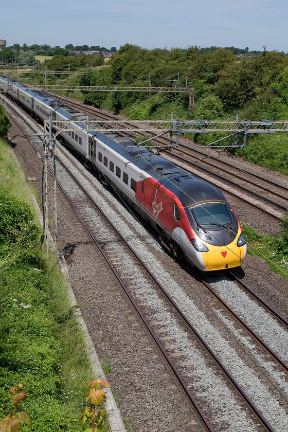 390011, VT 11.50 Birmingham New Street-London Euston (1B15, 1E), Victoria Bridge 
 The sun is just slightly too head-on for this shot but the Pendolino's bright 'flying scarf' livery just lifts the image enough. 390011 'City of Lichfield' races past Victoria Bridge between Roade and Ashton working the 11.50 Birmingham New Street to London Euston. 
 Keywords: 390011 1B15 Victoria Bridge