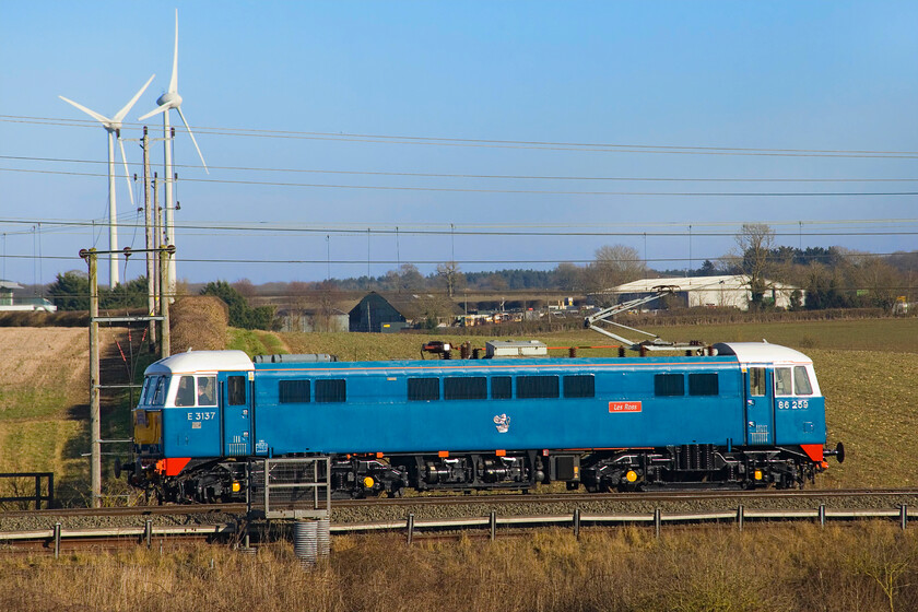 86259, 12.00 Acton Reception Sidings-Rugby CS (0Z86, 5E), Roade Hill 
 Having led another successful Cumbrian Mountain Express charter yesterday (apart from the steam-hauled section south over the Settle and Carlisle route) 86259 'Les Ross/Peter Pan' heads northwards near Roade as the 0Z86 12.00 Acton Reception Sidings to Crewe Carriage Sidings light engine move. Two turbines of the M1 windfarm dominate the skyline against a brilliant blue winter sky generating the same thing that the AL6 is running on! 
 Keywords: 862591 12.00 Acton reception Sidings-Rugby CS 0Z86 Roade Hill Les Ross Peter Pn