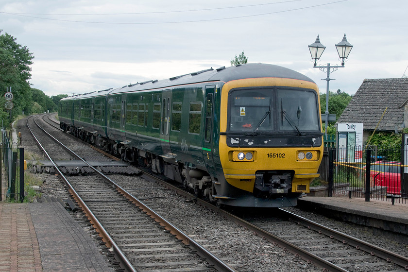 165102, GW 10.00 Didcot Parkway-Banbury (2M20, RT), Tackley station 
 Seen earlier at King's Sutton, 165102 is now arriving at Tackley station with the return 10.00 Didcot Parkway to Banbury Great Western service. Opened relatively late in 1931, Tackley station has basic facilities and is well maintained. It has no car parking facilities, something that residents probably curse as the roads leading to the station are narrow and somewhat inappropriate for the parking of cars; let's hope passengers are relatively local and make their way to the station by foot or bike. 
 Keywords: 165102 10.00 Didcot Parkway-Banbury 2M20 Tackely station