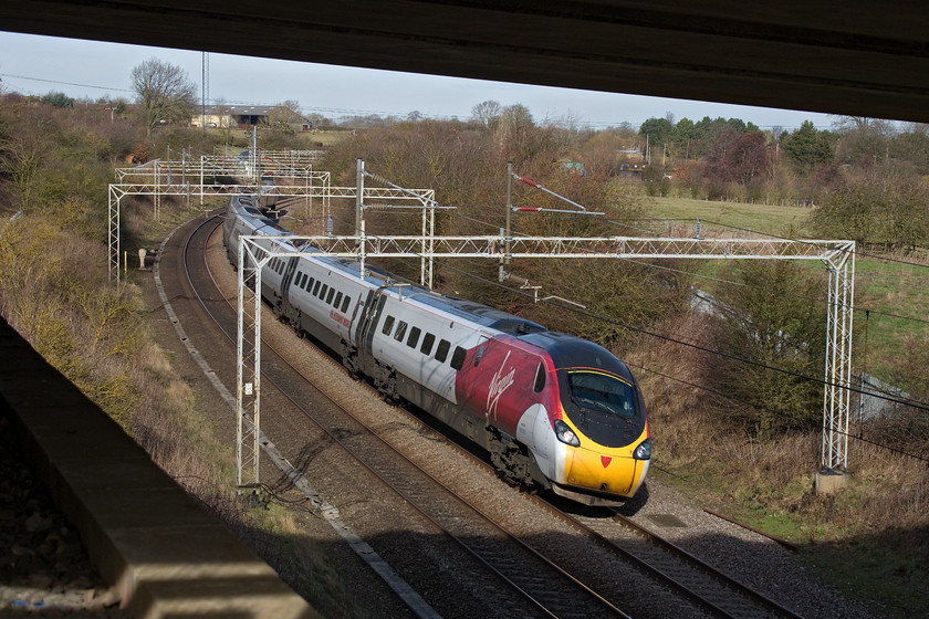 390039, VT 10.15 Manchester Piccadilly-London Euston (1A22, RT), A45 Weedon bypass bridge 
 I would not normally take a picture framed quite like this but I wanted to show the gradient of the bridge that carries the new A45 bypass climbs at around Weedon. Opened in December 2018, the road is climbing steeply here from its junction with the A5. 390039 sweeps around one of the reverse curves working the 10.15 Manchester Piccadilly to London Euston. After a cloudy start, it had turned into a glorious day with a hint of spring about it with temperatures reaching the dizzy heights of double figures! 
 Keywords: 390039 10.15 Manchester Piccadilly-London Euston 1A22 A45 Weedon bypass bridge