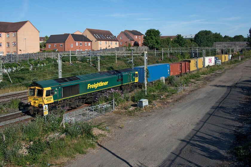 66592, 03.25 Garston-London Gateway (4L52, 3L), site of Roade station 
 Until recently taking a photograph from the footbridge that spans the WCML at the site of Roade's former station was easy with a low parapet on the eastward side at least. However, in their wisdom and in an attempt to spoil it for local children (and photographers for that matter) NR deemed it a safety-critical site and installed what appears to be polycarbonate parapet risers thus obliterating any view. Allegedly, this was due to incidents of school children climbing on the parapet. I have lived in the village for over fifteen years now and pass this spot almost daily at all times of the day and have never ever seen any such behaviour; another example of overzealous and ridiculous health and safety actions that will have cost us, the tax payers, yet more of our precious money - rant over! Taken now using my steps, 66592 'Johnson Stevens Agencies' passes the spot working the 4L52 03.25 Garston to London Gateway Freightliner service. 
 Keywords: 66592 03.25 Garston-London Gateway 4L52 site of Roade station Johnson Stevens Agencies