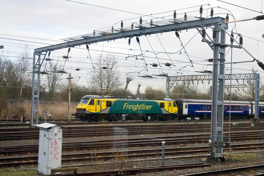 90045, stabled on sleeper stock, Wembley Yard 
 As the train I was travelling on entered Wembley Yard, 90045 is seen at the head of the sleeper stock. The class 90 had brought the empty sleeper stock out from Euston to Wembley for daytime servicing. The Freightliner looks very bright in its new Freightliner livery in the drab mid-winter weather. 
 Keywords: 90045 sleeper stock Wembley Yard