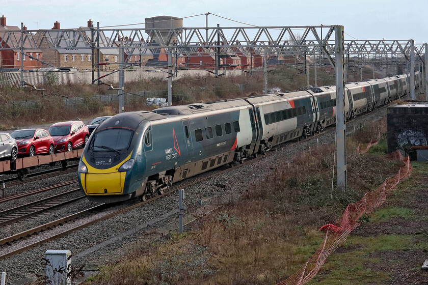 390107, VT 11.16 London Euston-Blackpool North (9P65, RT) & 09.28 Dagenham Docks-Garston Car Terminal (6X43, 24E), site of Roade station 
 As the 6X43 Dagenham Docks to Garston Ford train passes on the down slow line Avanti's 11.16 Euston to Blackpool North overtakes it on the fast line. Both trains are seen passing Roade in Northamptonshire with one of the village's two water towers standing in the background. 
 Keywords: 390107 11.16 London Euston-Blackpool North 9P65 09.28 Dagenham Docks-Garston Car Terminal 6X43 site of Roade station Ford AWC Avanti West Coast