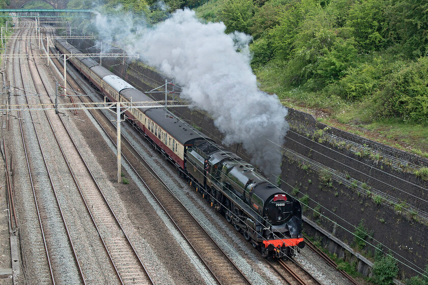 70000, outward leg of The Royal Charter, 07.18 Crewe-Windsor & Eton Riverside (1Z70, 5E), Roade cutting 
 70000 'Britannia' makes a fine sight as it climbs through Roade cutting having left Northampton some five minutes earlier. It is leading a set Saphos Train stock that left Crewe at 07.18 and was heading for Windsor and Eton Riverside station. Named the Royal Charter the train was running as 1Z70 in a nod number of years that Queen Elizabeth II had been on the throne. I chose this location as it was essentially a cloudy morning but just prior to the train's arrival the sun came out putting this side of the subject in shadow, however, with a bit of Photoshop tweaking a reasonable image has resulted. 
 Keywords: 70000 The Royal Charter, 07.18 Crewe-Windsor & Eton Riverside 1Z70 Roade cutting Britannia